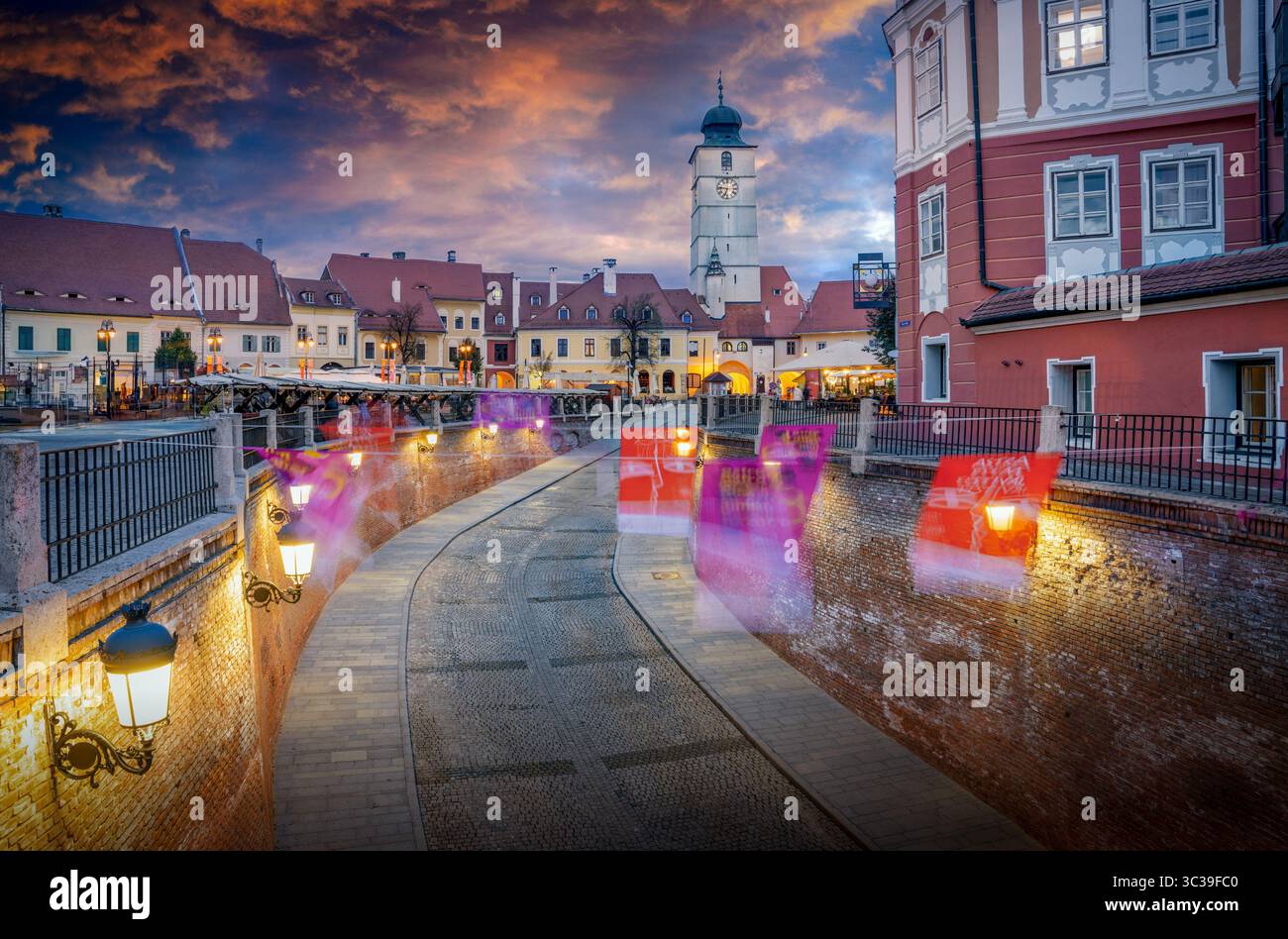 La tour historique du conseil (Turnul Sfatului) à Sibiu, en Roumanie, illuminée par la lueur chaude du coucher de soleil, avec des nuages oranges et un bleu saisissant Banque D'Images