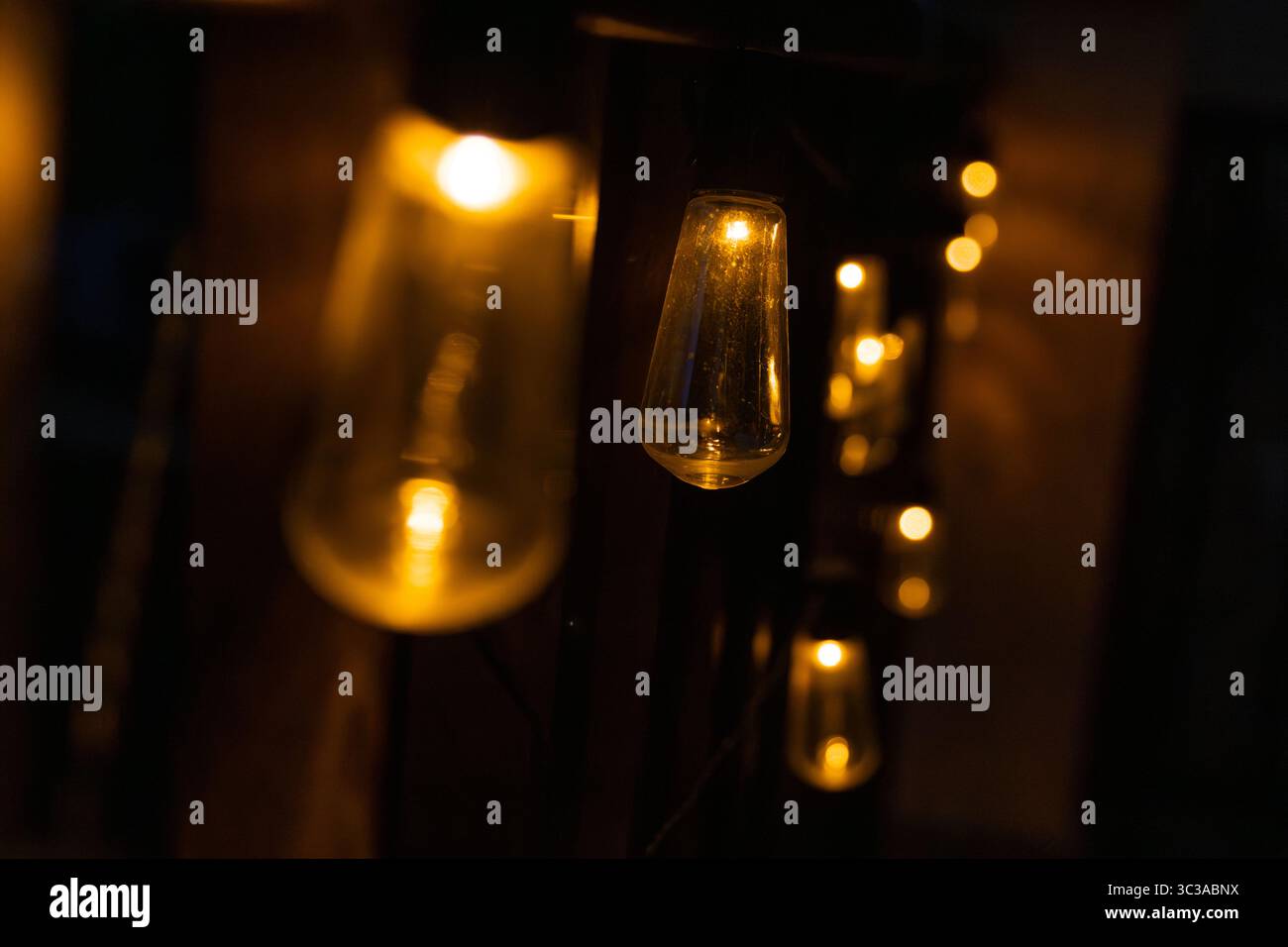 Chaîne d'ampoules aux tons chauds éclairant un espace sombre, créant une ambiance chaleureuse et accueillante Banque D'Images