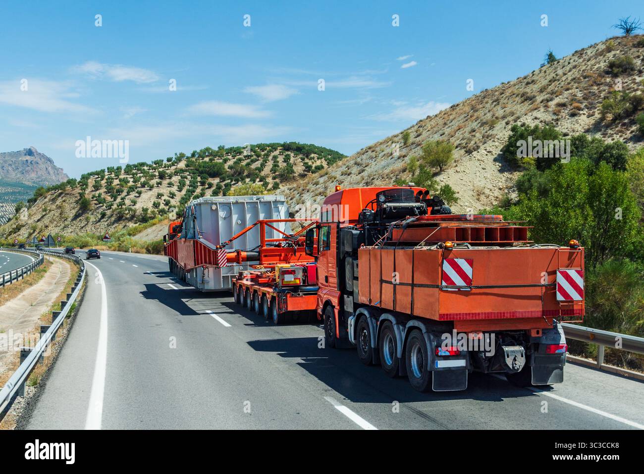 Camions lourds transportant une caisse métallique massive sur une pente raide, avec un camion devant et un autre derrière la charge. Vue arrière. Banque D'Images