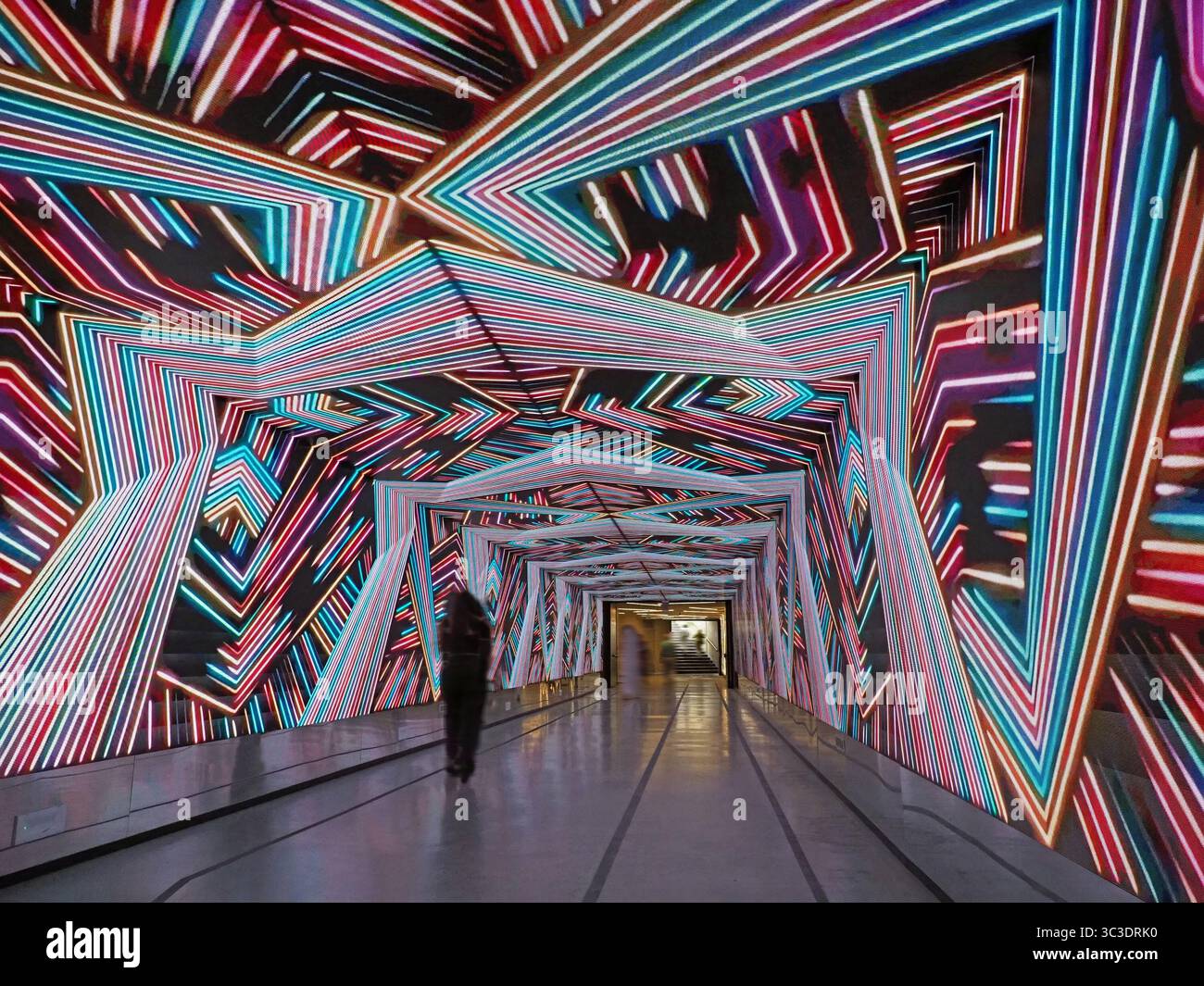 Figure anonyme au milieu d'un affichage d'éclairage électronique changeant psychédélique dans un tunnel souterrain dans le centre de Florence, en Italie Banque D'Images
