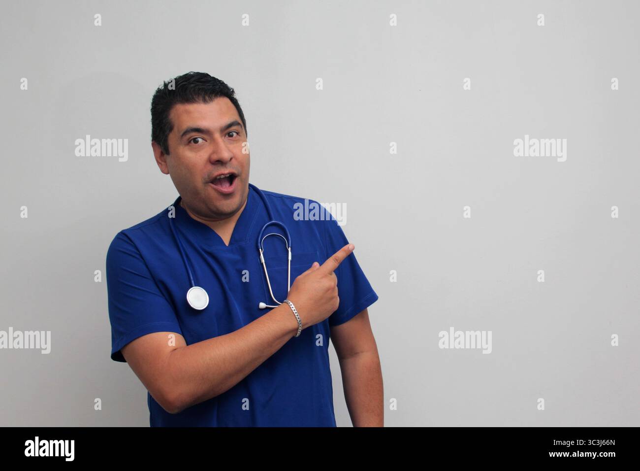 Médecin spécialiste latino-américain à la peau foncée avec un stéthoscope pointe avec son doigt avec une expression de joie et de surprise Banque D'Images Médecin spécialiste latino-américain à la peau foncée avec un stéthoscope pointe avec son doigt avec une expression de joie et de surprise Banque D'Images