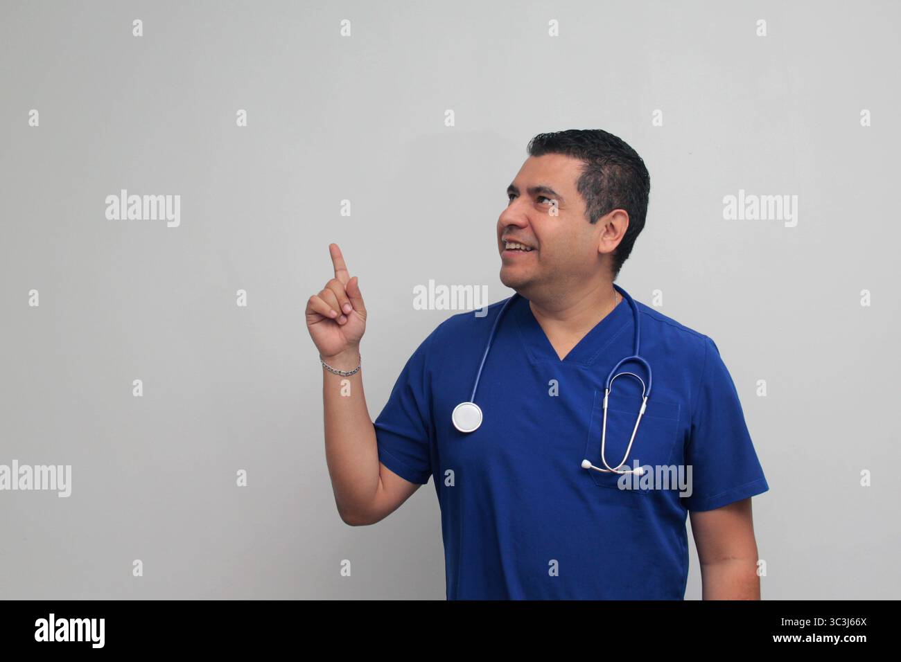 Médecin spécialiste latino-américain à la peau foncée avec un stéthoscope pointe avec son doigt avec une expression de joie et de surprise Banque D'Images Médecin spécialiste latino-américain à la peau foncée avec un stéthoscope pointe avec son doigt avec une expression de joie et de surprise Banque D'Images