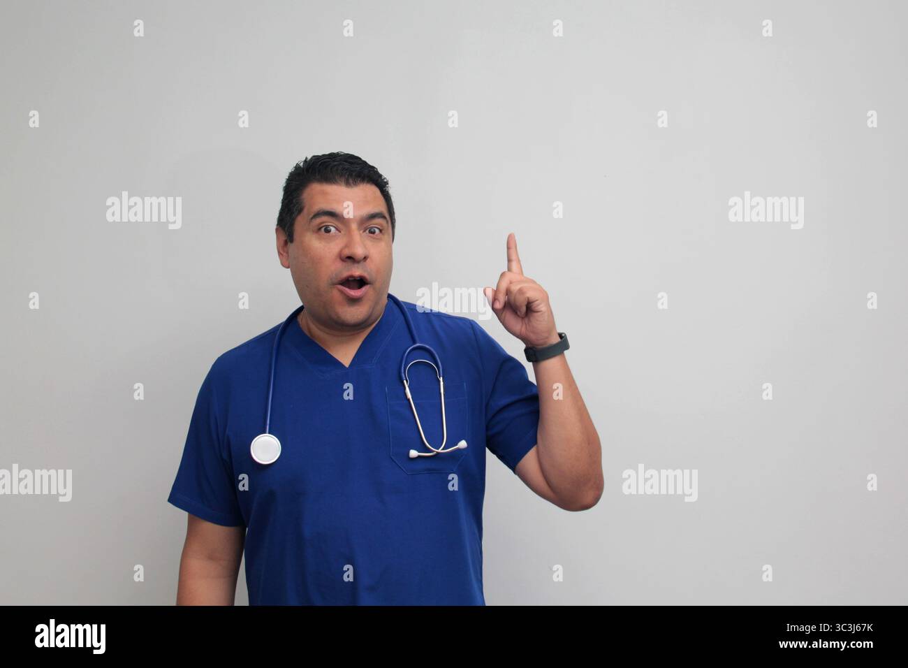 Médecin spécialiste latino-américain à la peau foncée avec un stéthoscope pointe avec son doigt avec une expression de joie et de surprise Banque D'Images Médecin spécialiste latino-américain à la peau foncée avec un stéthoscope pointe avec son doigt avec une expression de joie et de surprise Banque D'Images