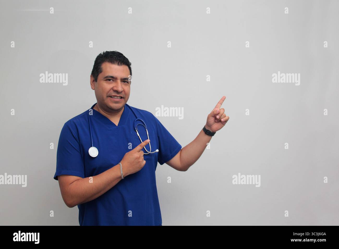Médecin spécialiste latino-américain à la peau foncée avec un stéthoscope pointe avec son doigt avec une expression de joie et de surprise Banque D'Images Médecin spécialiste latino-américain à la peau foncée avec un stéthoscope pointe avec son doigt avec une expression de joie et de surprise Banque D'Images
