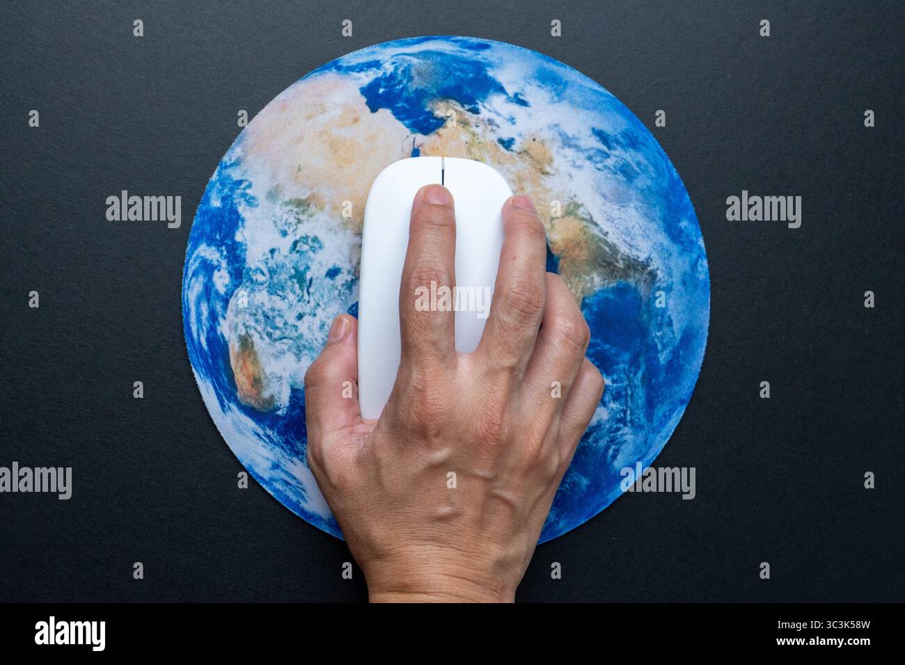 Une main actionnant une souris d'ordinateur sur un tapis de souris rond présentant une carte détaillée de la Terre. Connectivité mondiale, communication numérique et impact Banque D'Images