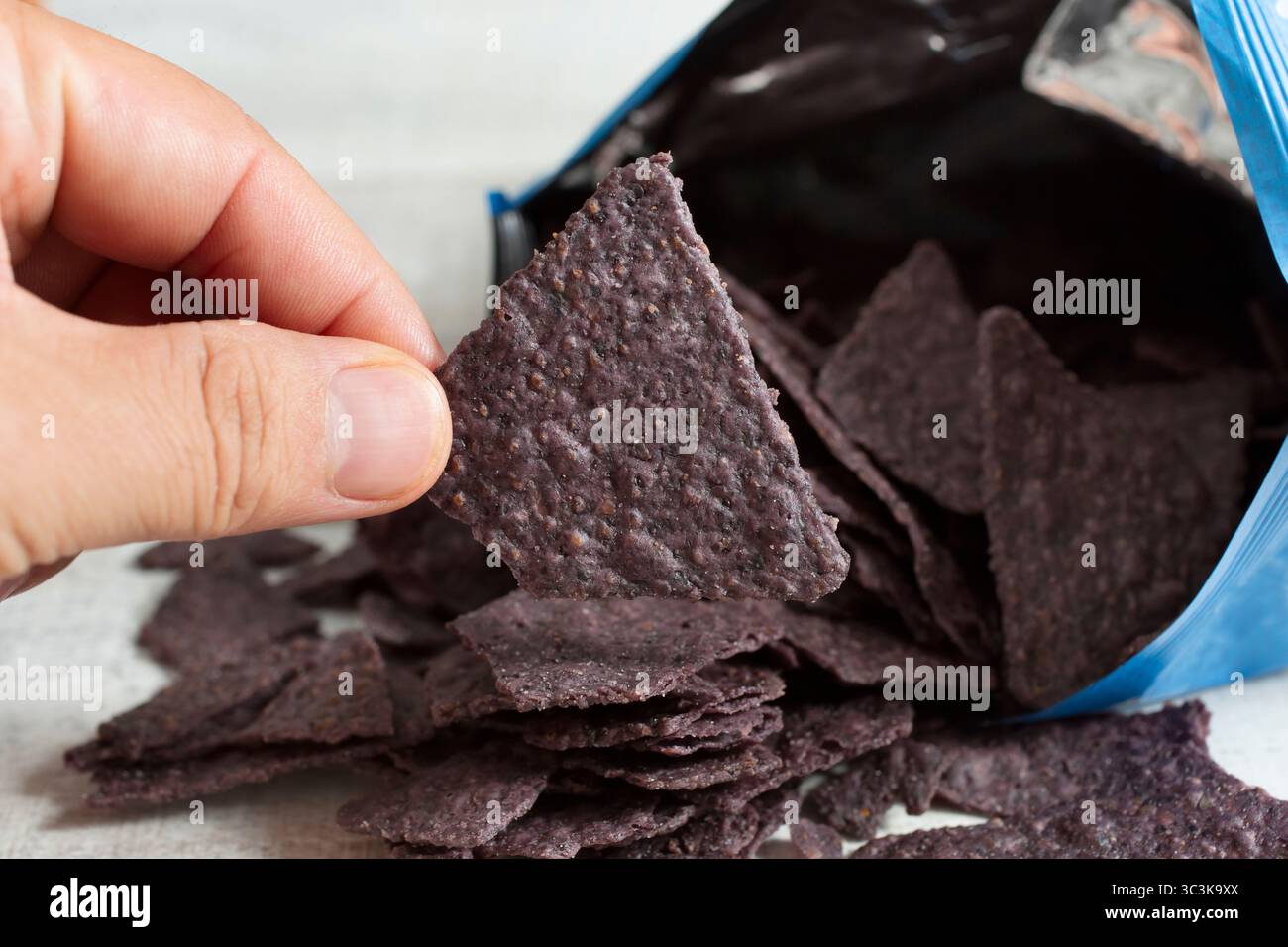 Une vue d'une main tenant une seule puce de tortilla de maïs bleue. Banque D'Images