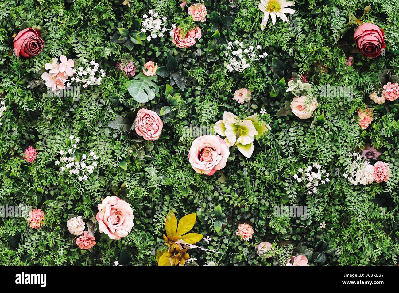 Fond artificiel de mur de fleur. Roses et feuilles colorées. Verdure décorative avec fleurs en plastique. Concept de décoration événementielle. Plantes fausses luxuriantes. Banque D'Images