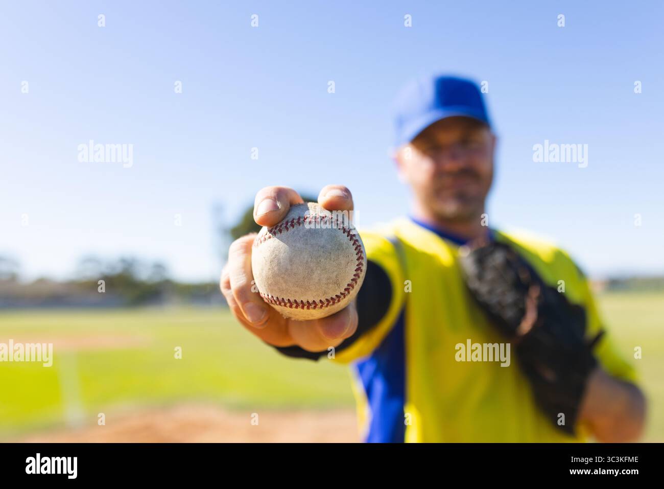 Baseball blanc tenu vers la caméra avec un gant noir reposant sur le terrain de baseball sous le ciel bleu Banque D'Images
