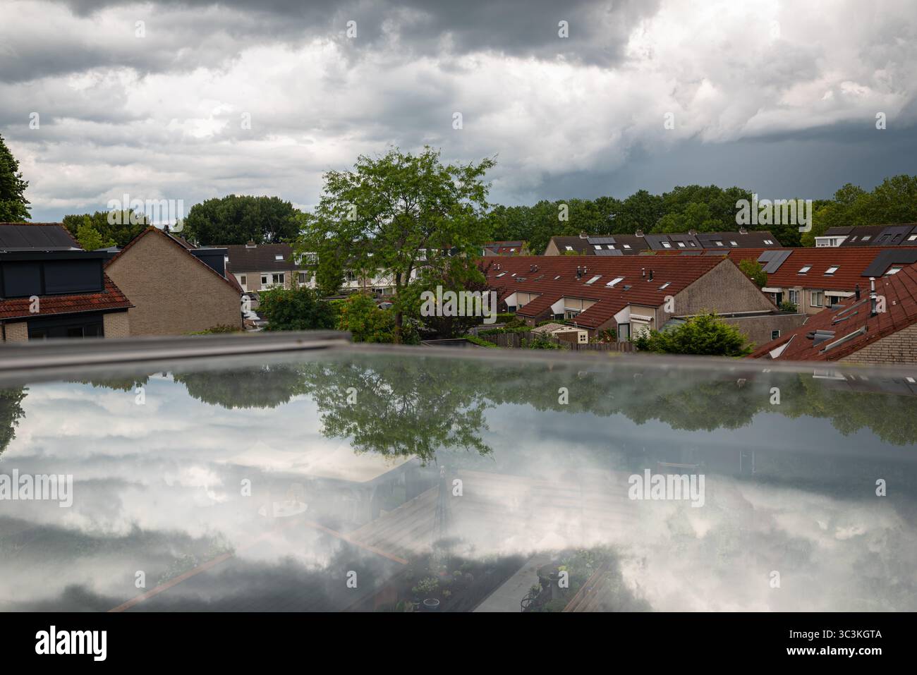 Une vue panoramique d'un quartier de banlieue avec des toits de tuiles, de la verdure et des reflets sur une surface vitrée sous un ciel couvert. Banque D'Images