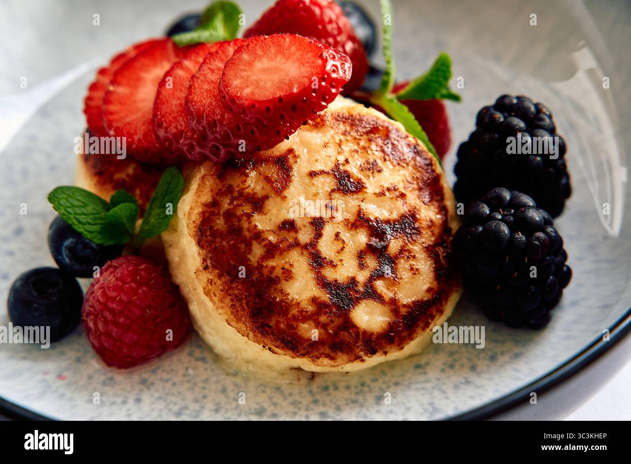 Une délicieuse assiette de crêpes moelleuses garnie de baies fraîches, y compris des fraises, des framboises et des bleuets, garnie de feuilles de menthe pour un Banque D'Images