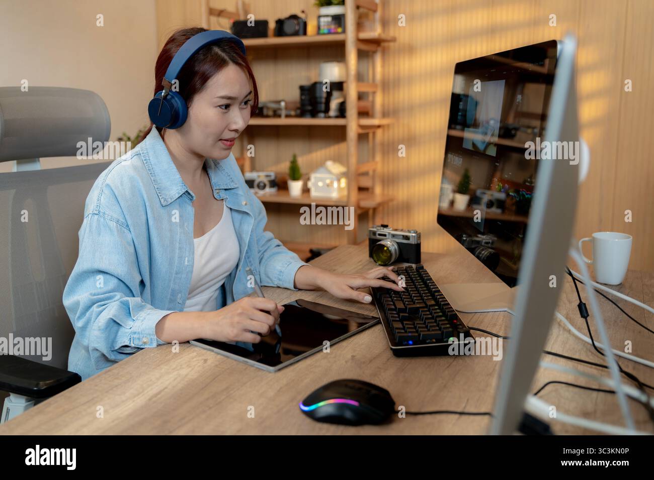 Une jeune monteuse vidéo indépendante souriante travaillant sur un ordinateur portable à la maison, profitant de son travail créatif dans un environnement détendu. Banque D'Images