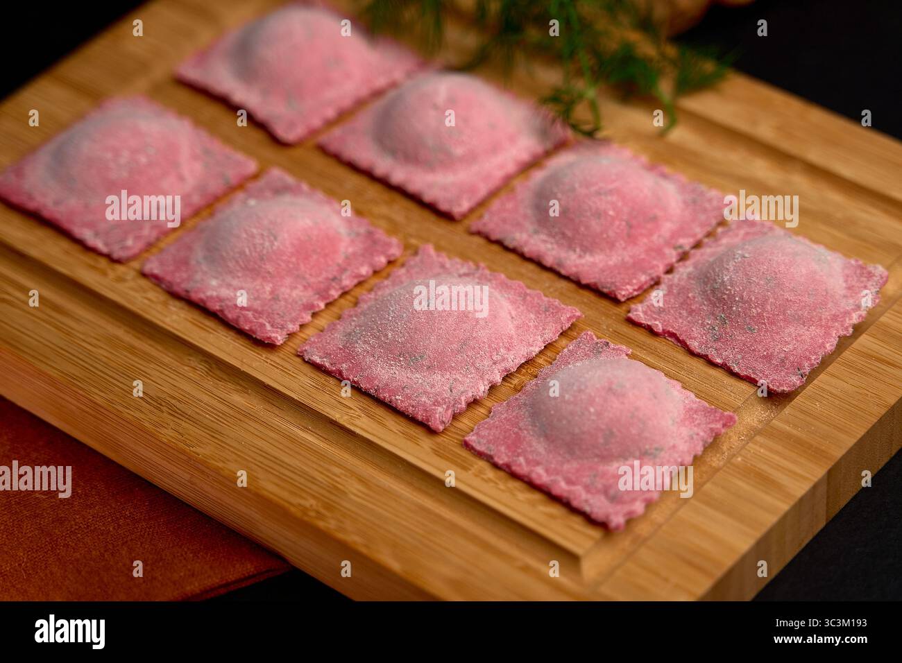 Raviolis faits maison colorés sur une planche en bois prête pour la cuisson, présentant une teinte rose unique et une qualité artisanale pour la préparation de repas gastronomiques Banque D'Images