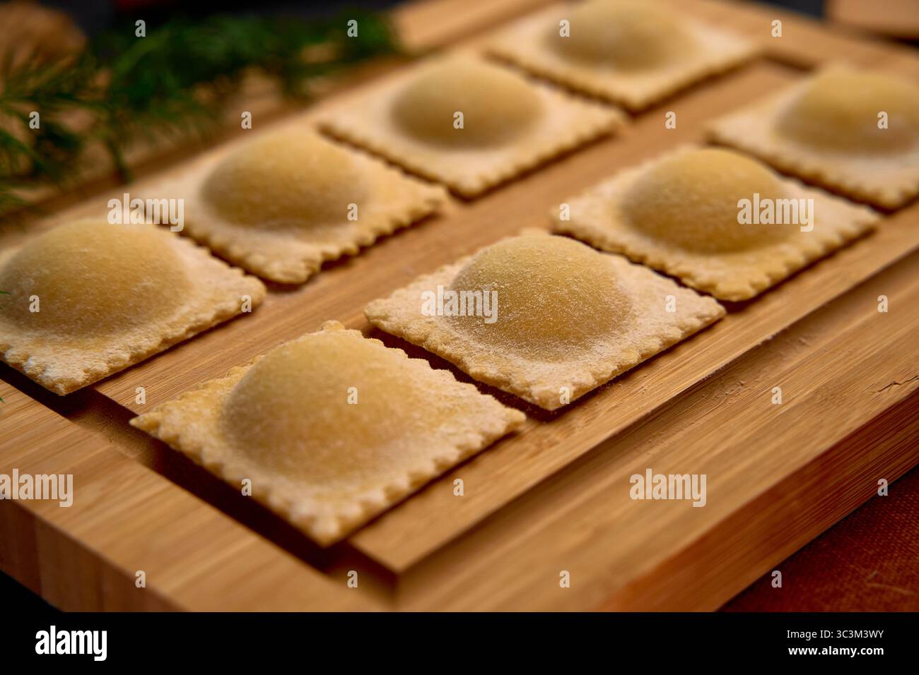 Délicieux raviolis de pâtes faits à la main se préparant pour la cuisson avec une belle garniture entourée d'ingrédients frais sur une planche en bois Banque D'Images
