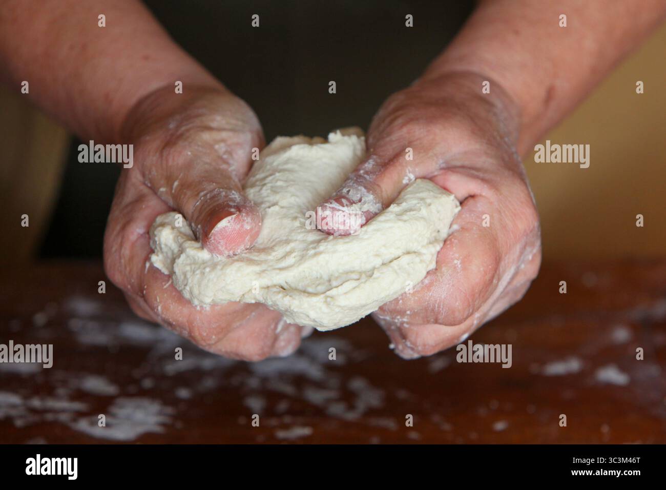 gros plan des mains d'une femme âgée, vêtue de façon désinvolte à la maison, faisant de la pâte à la main sur une table rustique en bois simple Banque D'Images