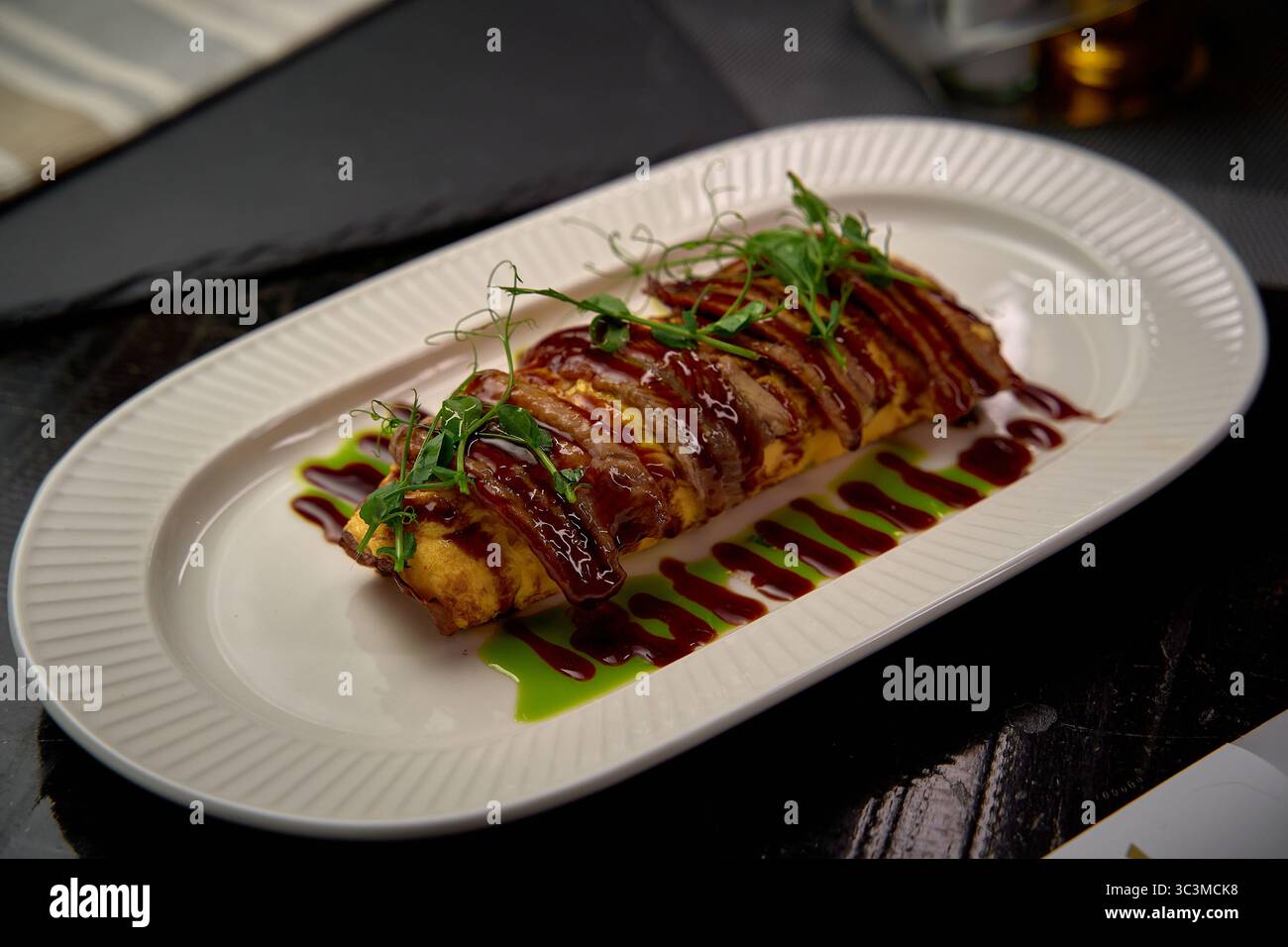 Une assiette d'omelette gastronomique magnifiquement présentée arrosée de sauce riche et garnie d'herbes fraîches, mettant en valeur l'art culinaire et l'élégance du di Banque D'Images
