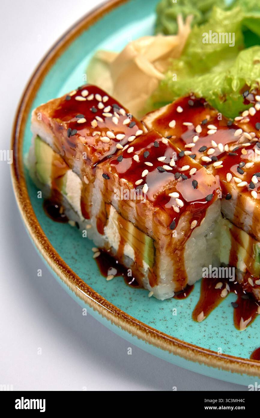Délicieux rouleaux de sushi avec une riche sauce anguille, des graines de sésame et des légumes verts frais servis sur une assiette turquoise vibrante, parfait pour les amateurs de cuisine et de cuisine Banque D'Images