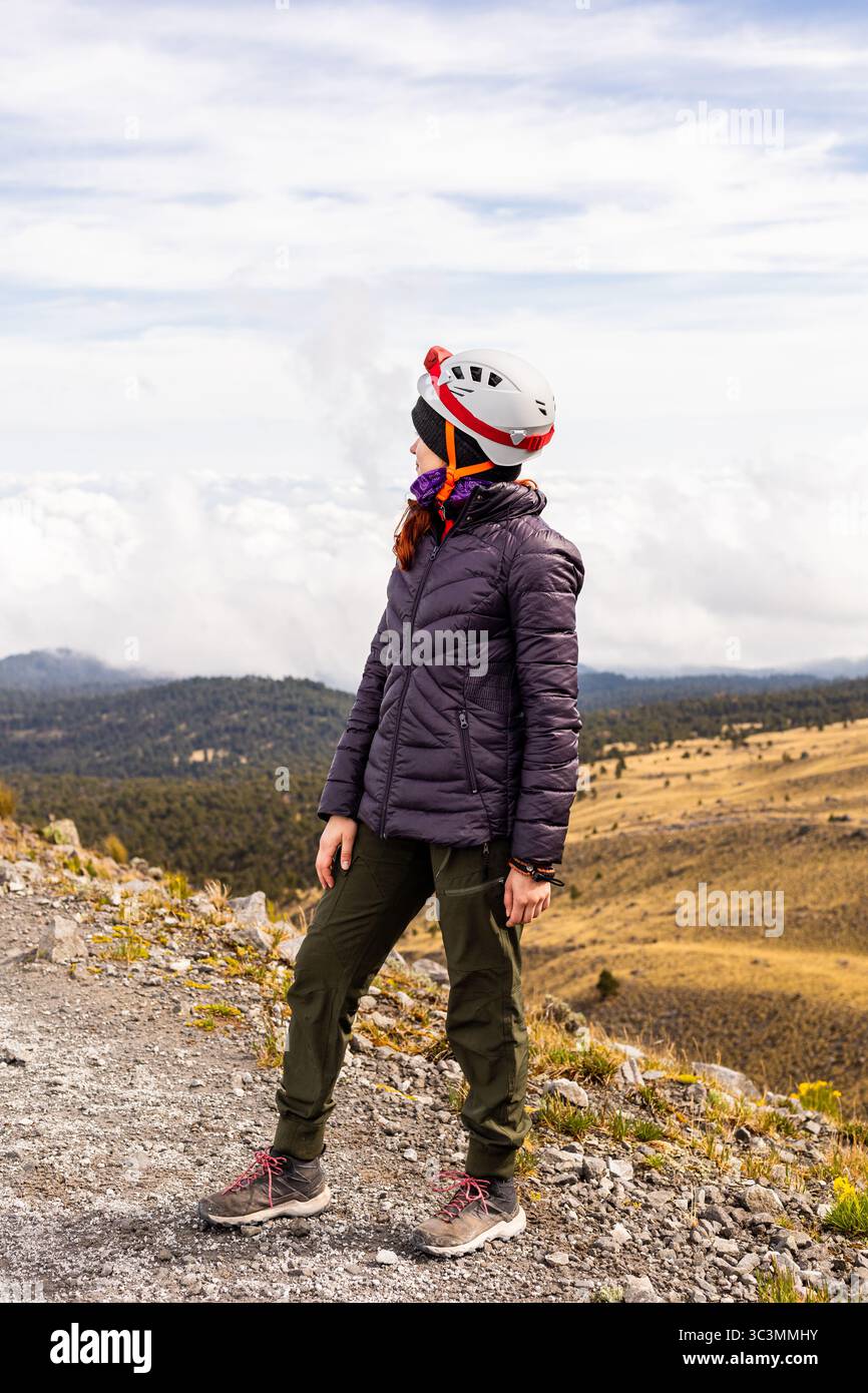 Une femme en équipement de randonnée se tient sur un sentier rocheux, embrassant le paysage de montagne à couper le souffle. Sa position reflète l'aventure et la liberté, tandis que le va Banque D'Images