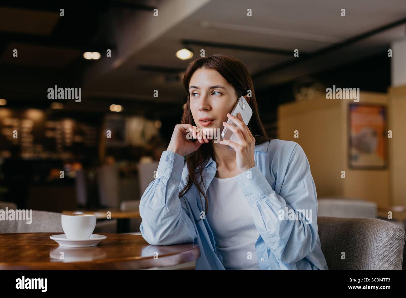 Une femme professionnelle s'engage dans un appel téléphonique alors qu'elle est assise dans un café confortable, mettant en valeur un mélange de travail et de détente. Une tasse de café est posée sur la table Banque D'Images