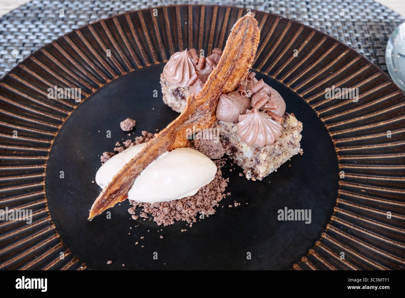 Assiette à dessert élégante avec des bouchées de gâteau au chocolat recouvertes d'une mousse riche et garnies d'un éclat de chocolat croustillant, accompagné d'une quenelle de Banque D'Images