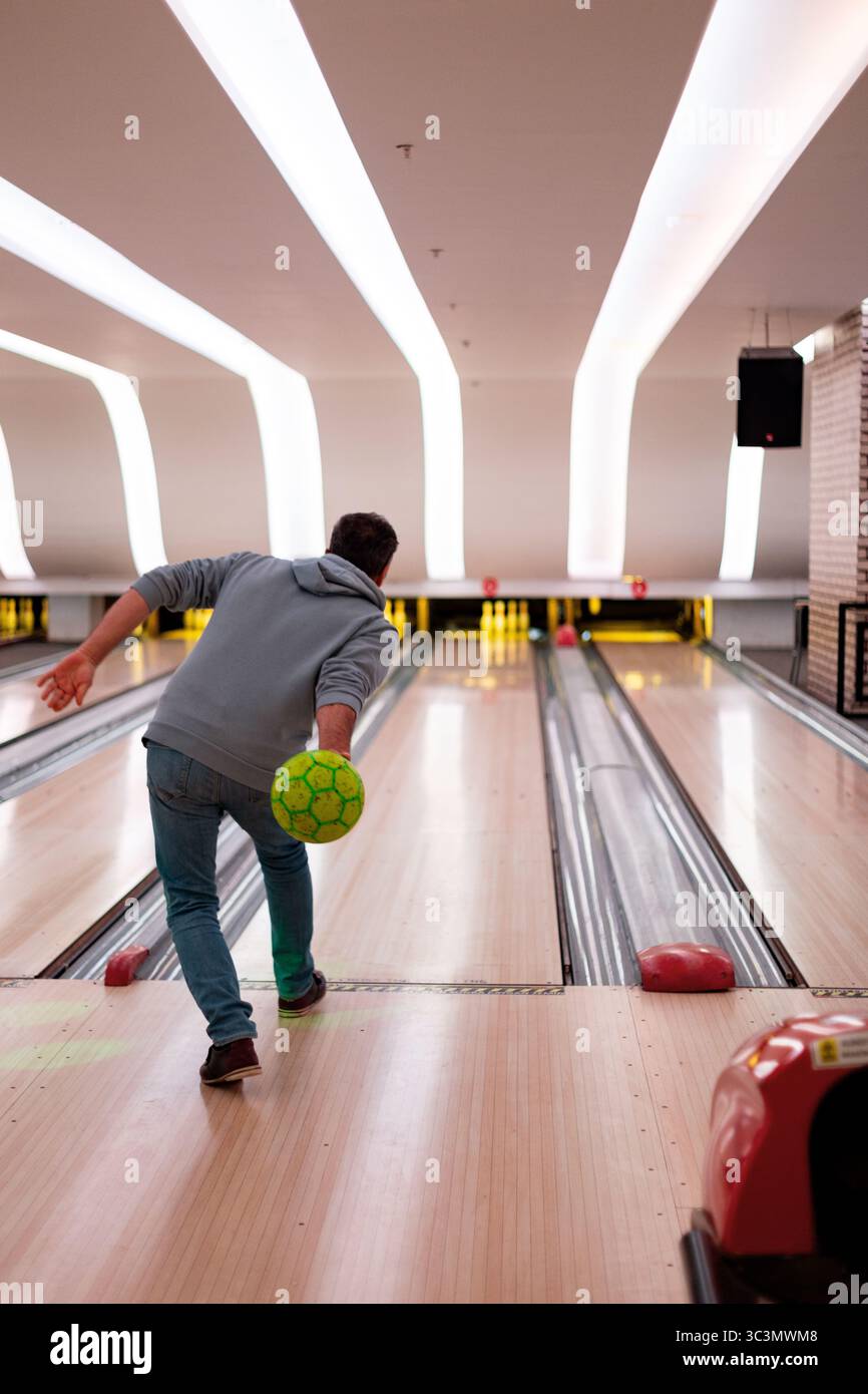 Un père est capturé en pleine action, jouant habilement au bowling dans une ruelle moderne bien éclairée. Il se concentre sur le jeu, mettant en valeur la précision et la technique comme il l'ai Banque D'Images