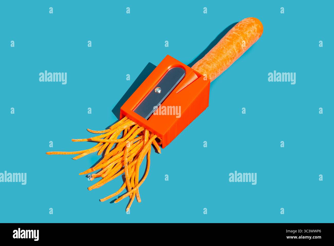 Un taille-crayon orange coupe artistiquement une carotte en fines mèches sur un fond bleu éclatant. L'image mélange créativité et quotidien Banque D'Images