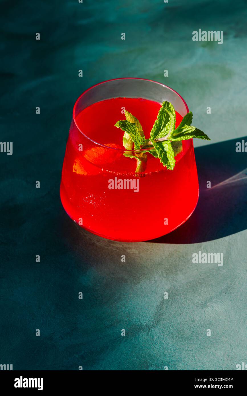 D'en haut un thé d'été froid rafraîchissant infusé de fraises et d'hibiscus, garni de feuilles de menthe fraîche. La boisson rouge éclatante est illuminée Banque D'Images