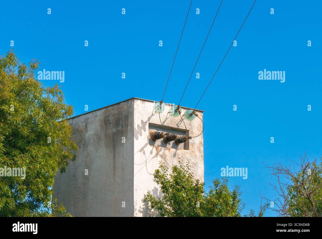 Une vieille boîte de transformateur électrique en béton avec du matériel électrique et des lignes électriques se trouve à l'extérieur entouré d'arbres verts sous un clair, CLO Banque D'Images