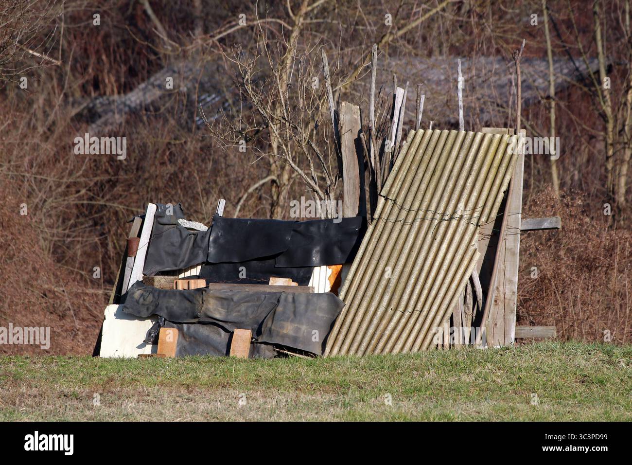 Des clôtures improvisées de feuilles ondulées, de planches de bois et de matériaux altérés se dressent sur l'herbe, mettant en valeur l'ingéniosité rurale et la construction recyclée Banque D'Images