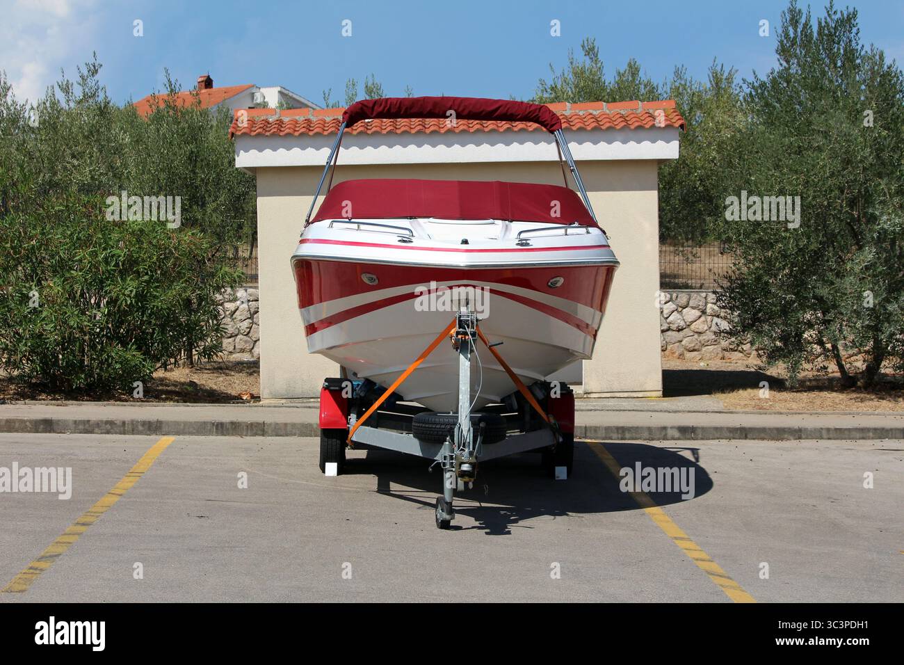Un hors-bord blanc et rouge avec un auvent rouge équipé est fixé sur une remorque dans un parking marqué, prêt pour le transport terrestre près d'un petit Banque D'Images