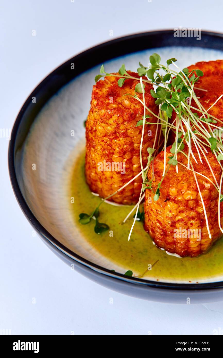 Maïs délicieusement carbonisé sur l'épi accompagné de Microgreens frais servis dans un bol, mettant en valeur l'art culinaire et la présentation gastronomique Banque D'Images