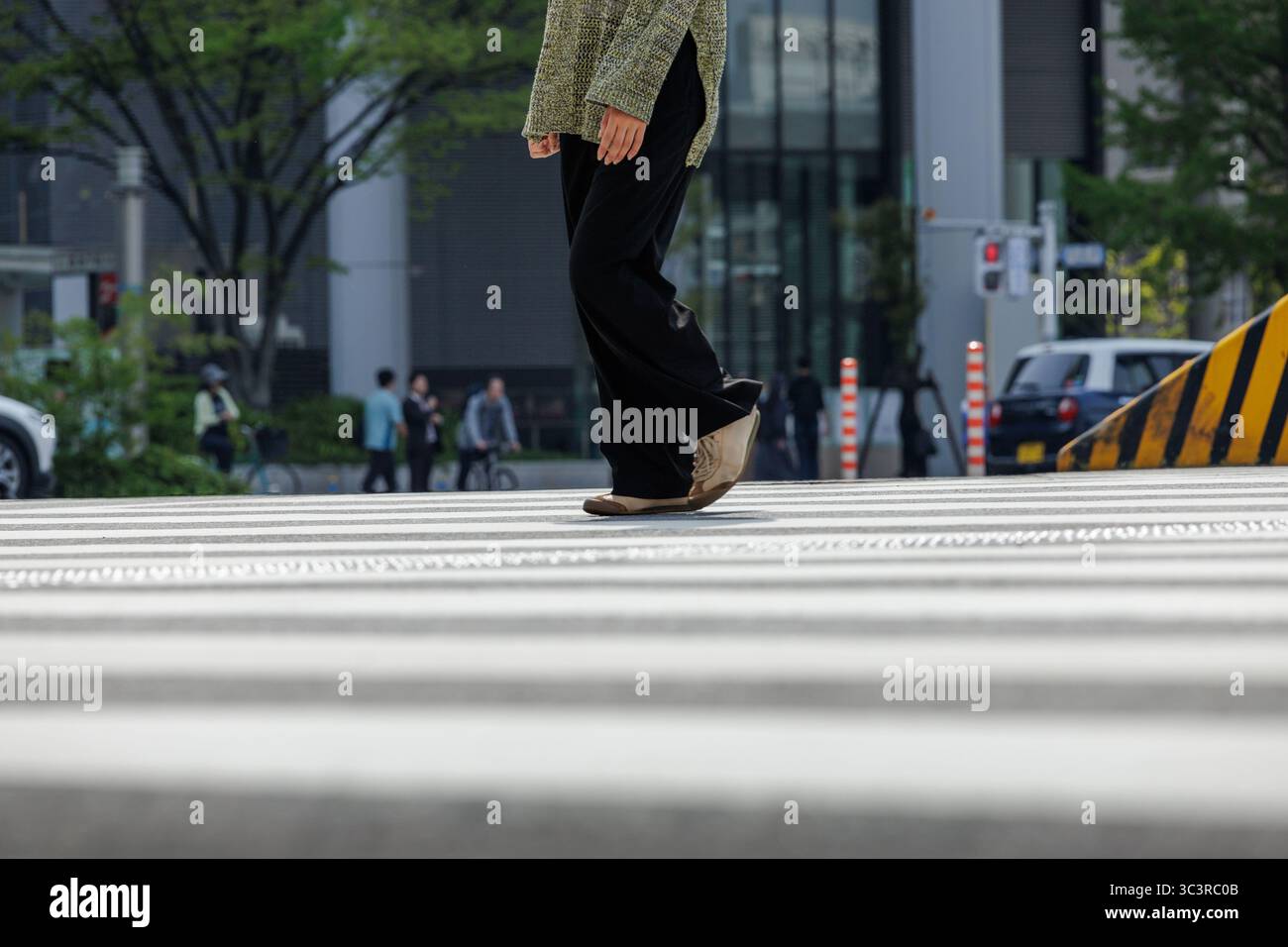 Personne à angle bas dans la croix zébrée, décontractée vêtue d'un pull vert mousse surdimensionné à la mode, d'un pantalon noir et de baskets à lignes fines à la mode. Banque D'Images