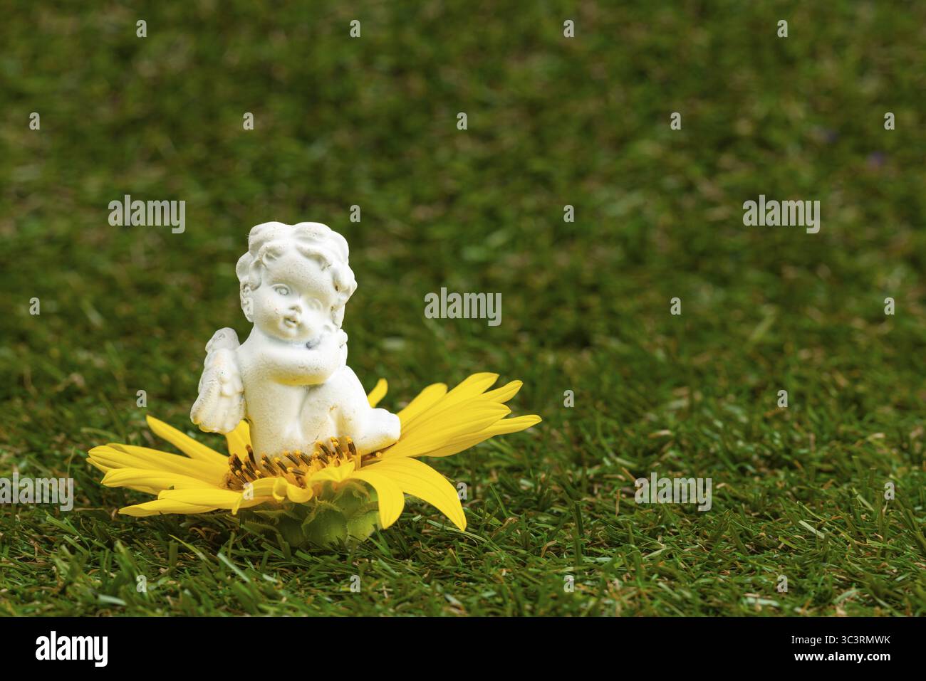 Petite figure d'ange assis sur une fleur jaune sur une pelouse verte Banque D'Images