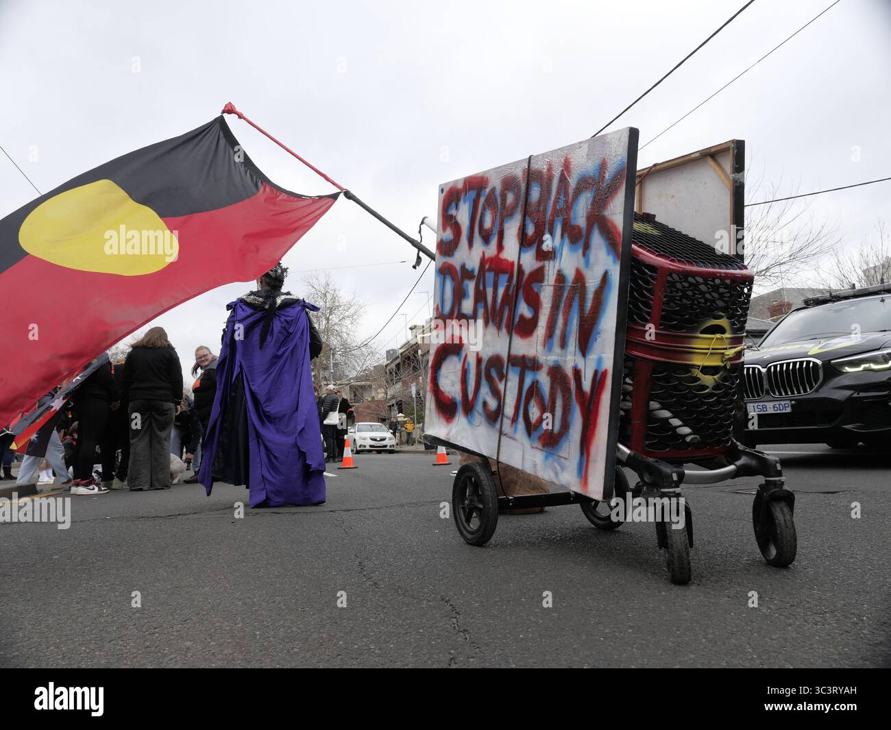 Le drapeau aborigène volant dans le vent est attaché à un tableau peint en blanc pour « arrêter les morts noires en détention » peint dessus lors de la marche NAIDOC à Melbourne Banque D'Images