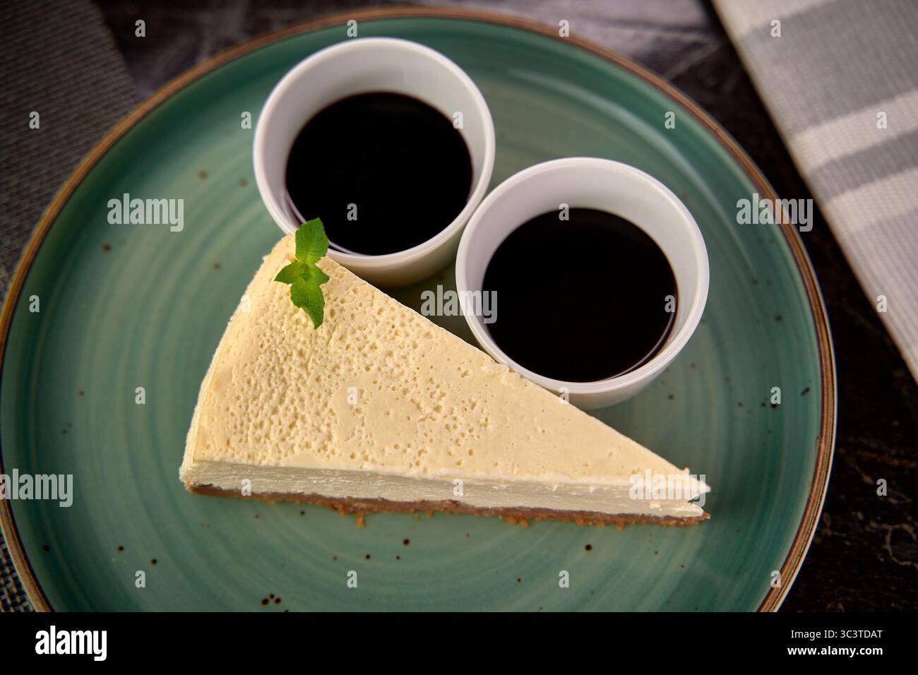 Délicieuse tranche de cheesecake crémeuse servie avec une riche sauce au chocolat dans de petites tasses blanches sur une assiette élégante Banque D'Images