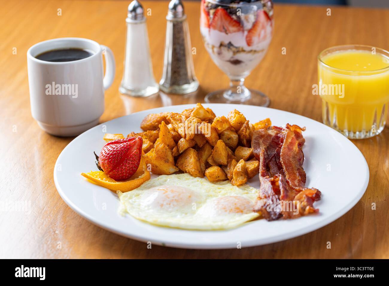 Copieux petit déjeuner avec pommes de terre dorées, bacon croustillant et fruits frais servis avec café chaud et jus d'orange. Repas de confort parfait le matin. Banque D'Images