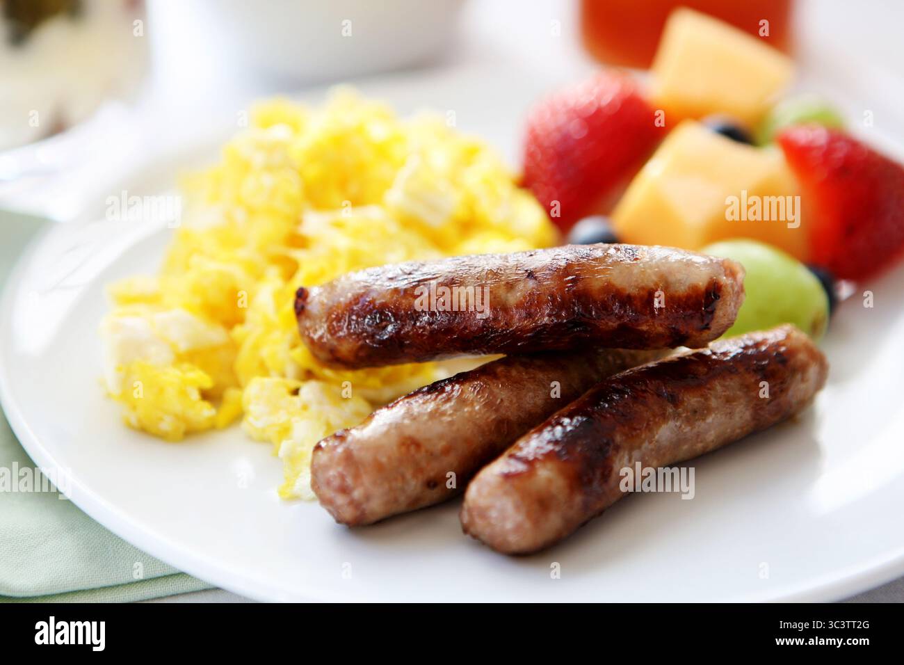 Saucisses grillées avec œufs brouillés moelleux et poivrons colorés sur assiette blanche. Copieux repas du matin protéiné plat de confort. Banque D'Images
