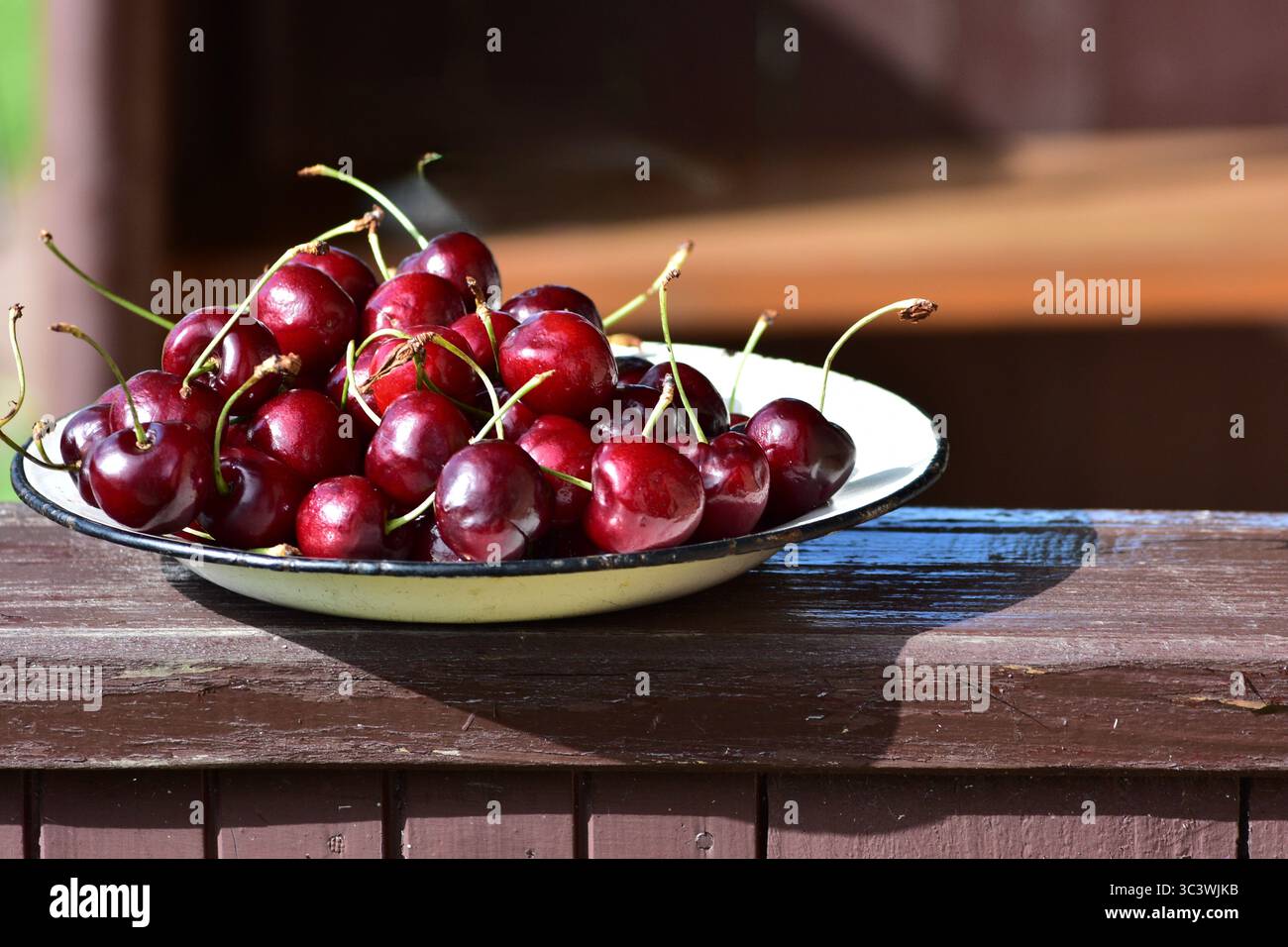 Assiette remplie de cerises mûres fraîchement cueillies sur une surface en bois. Fruits rouges juteux scintillant à la lumière naturelle, soulignant la récolte d'été et l'organi Banque D'Images