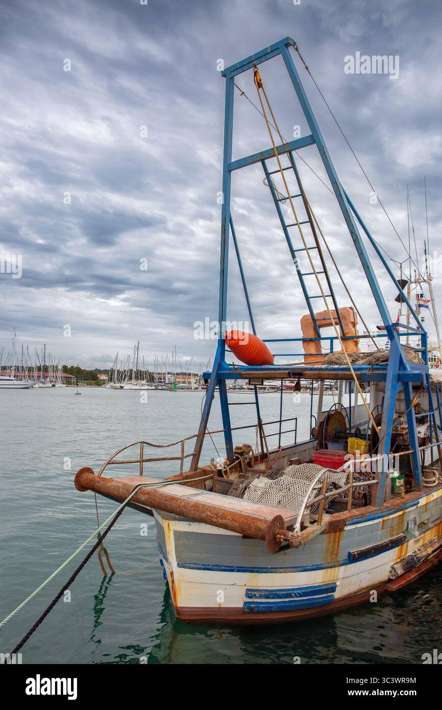 Vieux bateau de pêche traditionnel avec filets et équipement amarré à la marina de Novigrad en Istrie, Croatie. Grue de levage bleue et voiliers visibles en b Banque D'Images