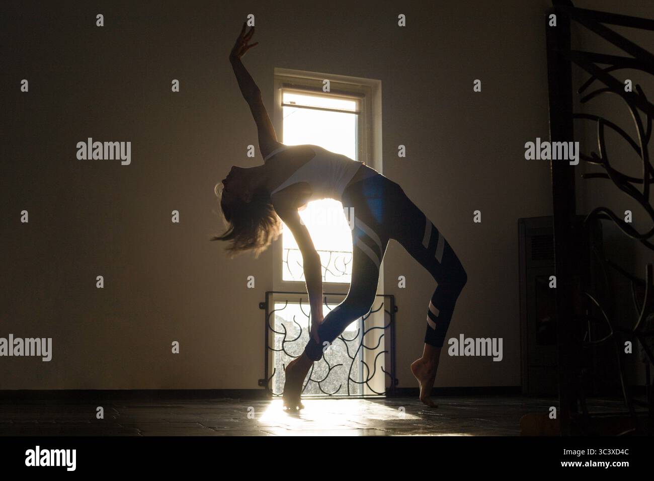 Femme sportive mince faisant la danse spectaculaire de bande arrière devant la fenêtre, où viennent la lumière du soleil dorée. Routine de yoga matinale, danse, soins personnels, AC Banque D'Images