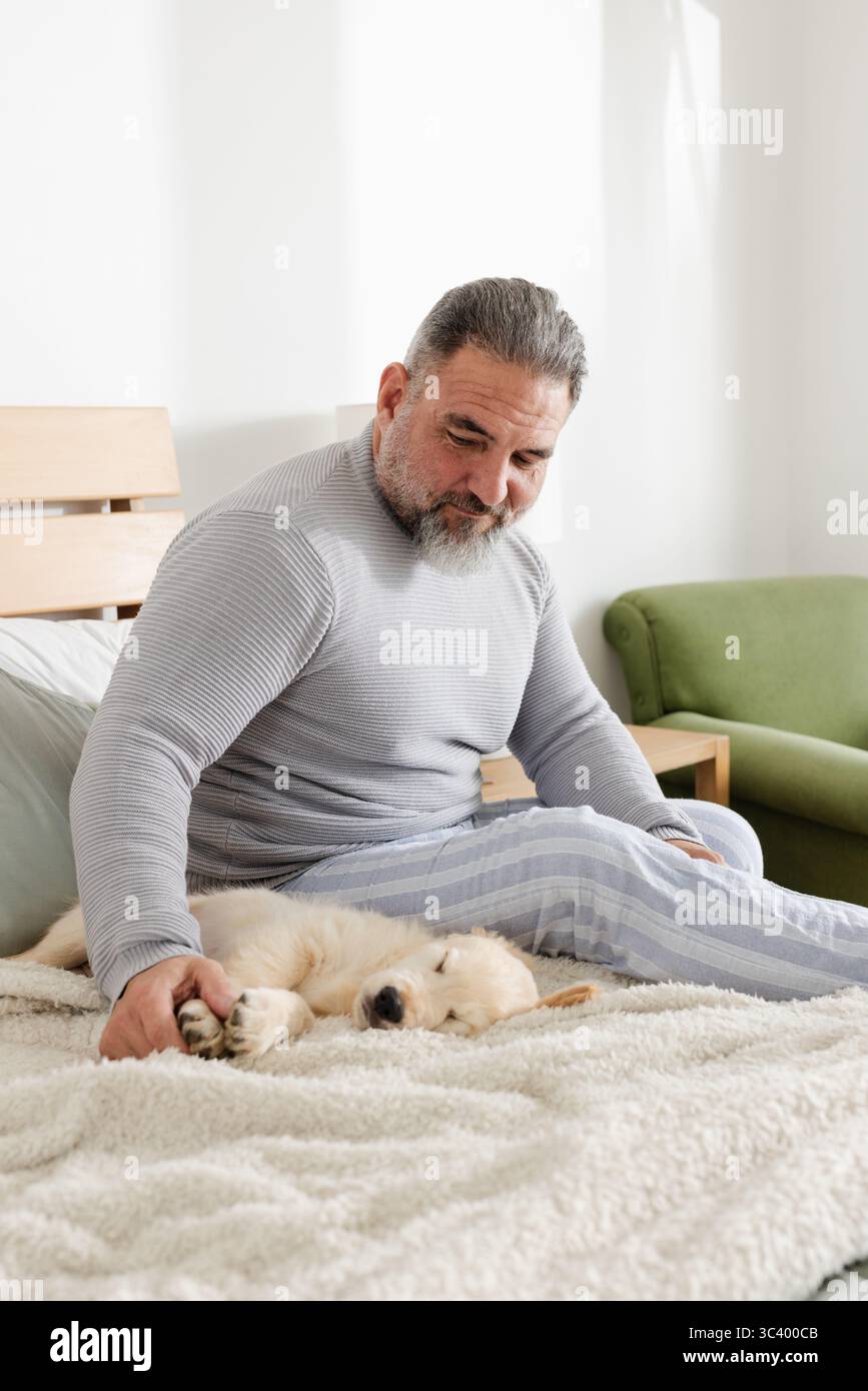 Homme senior portant un pull gris et un pyjama rayé assis sur le lit dans la chambre chiot d'enfant Banque D'Images Homme senior portant un pull gris et un pyjama rayé assis sur le lit dans la chambre chiot d'enfant Banque D'Images