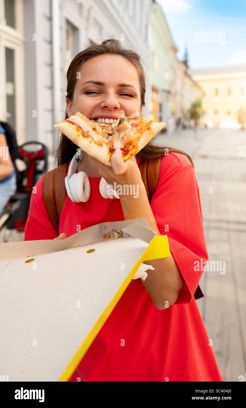 Heureuse étudiante mangeant de la pizza dans la rue de la ville Banque D'Images