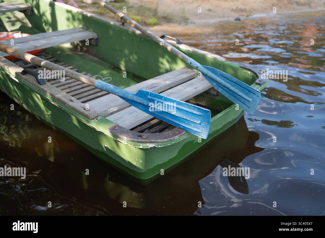 Un bateau vert vibrant équipé de deux rames bleues saisissantes flotte doucement dans l'eau, créant une scène pittoresque Banque D'Images