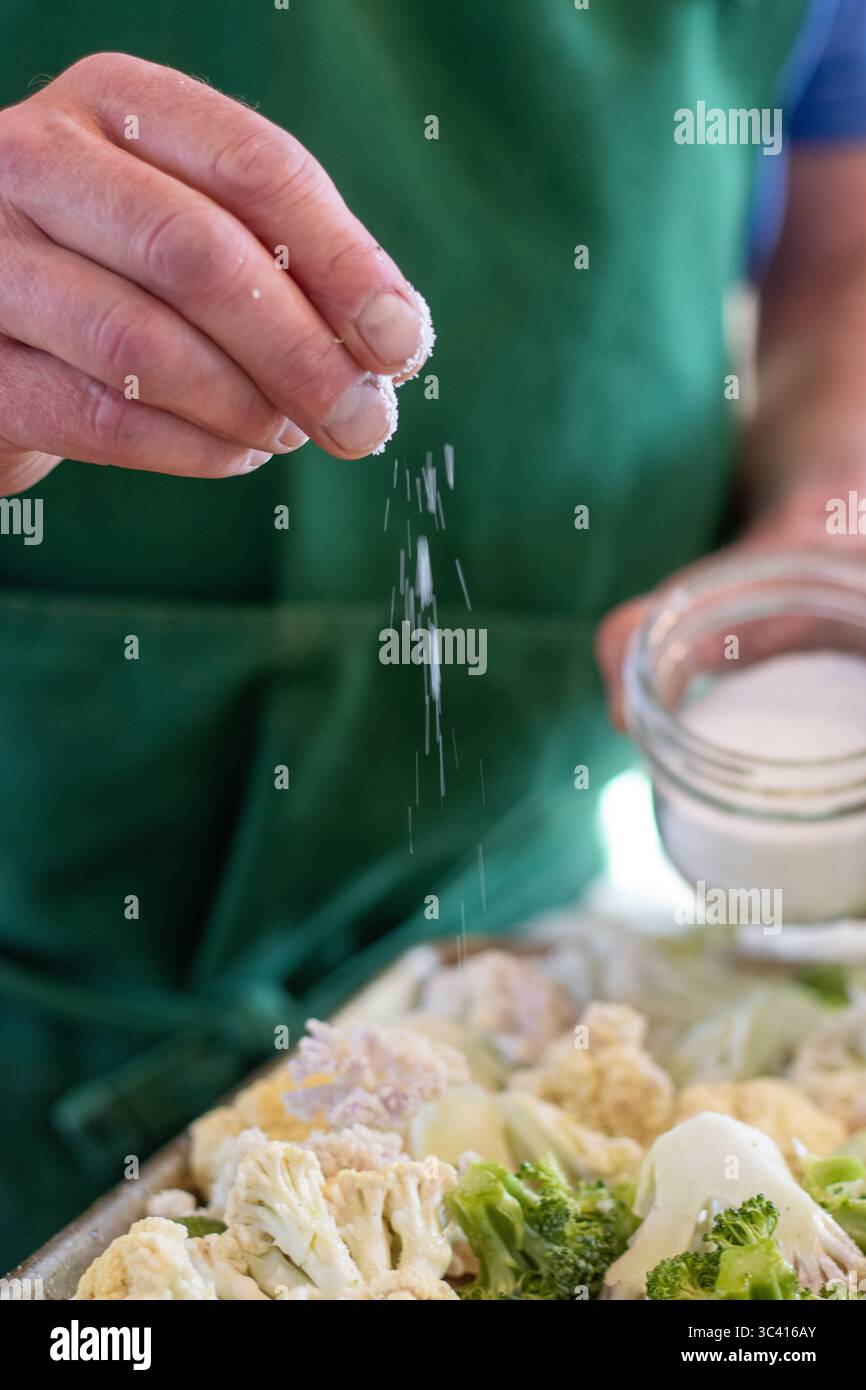 Saupoudrer à la main du gros sel sur les légumes frais du jardin Banque D'Images
