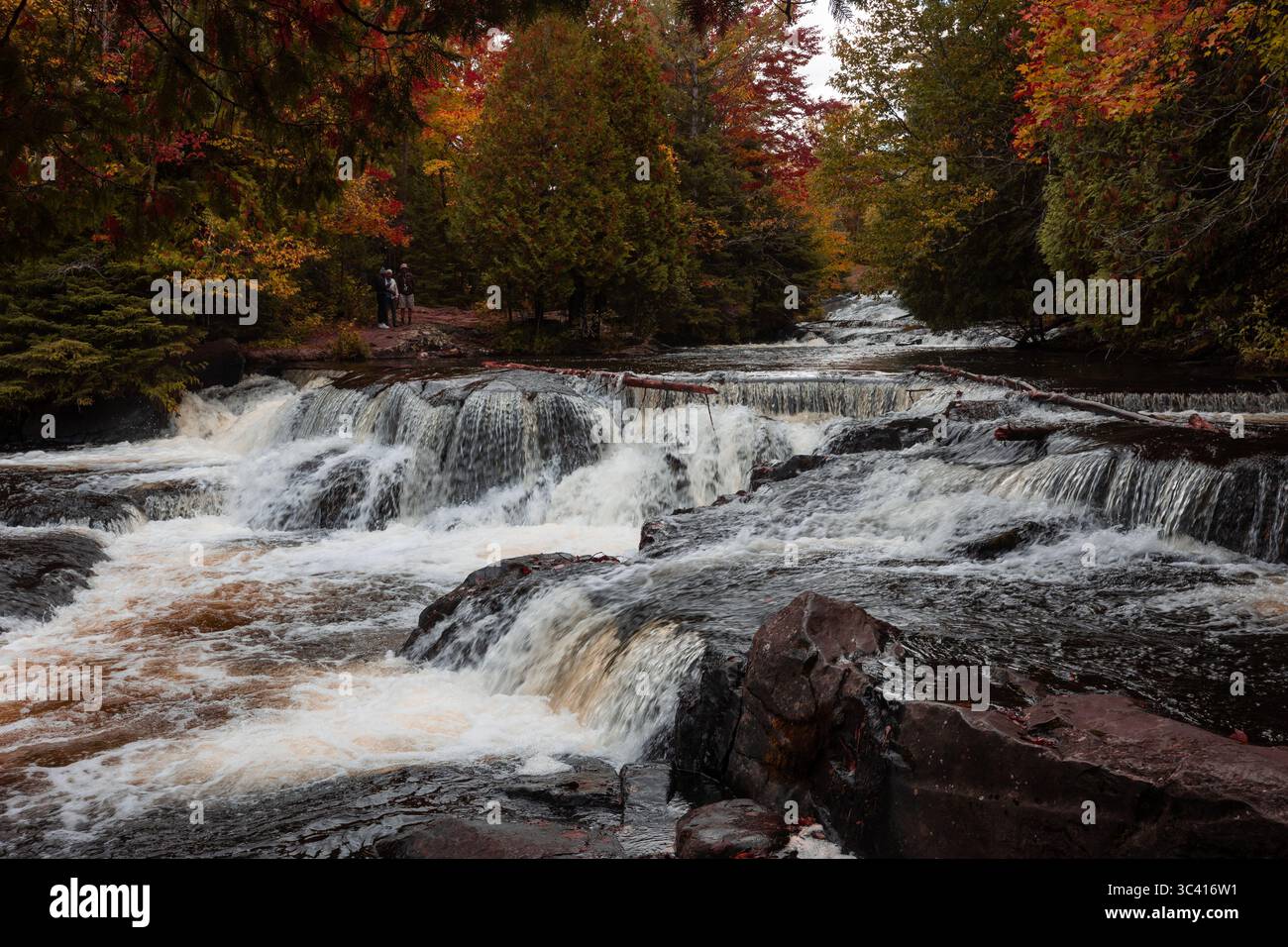 Cascade à plusieurs niveaux avec arbres d'automne et randonneurs à proximité. Banque D'Images