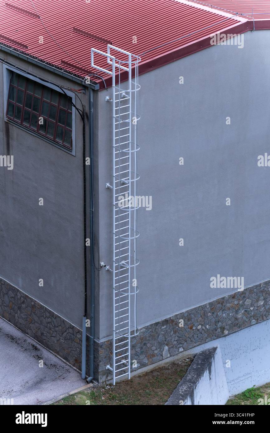 Échelles en métal blanc sur mur gris et toiture en étain rouge – autour du coin Banque D'Images