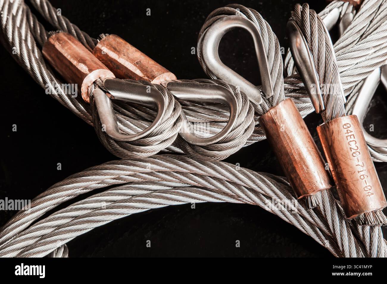 Câble en acier inoxydable, avec boucles et pinces en cuivre, et un fond noir, gros plan. Banque D'Images