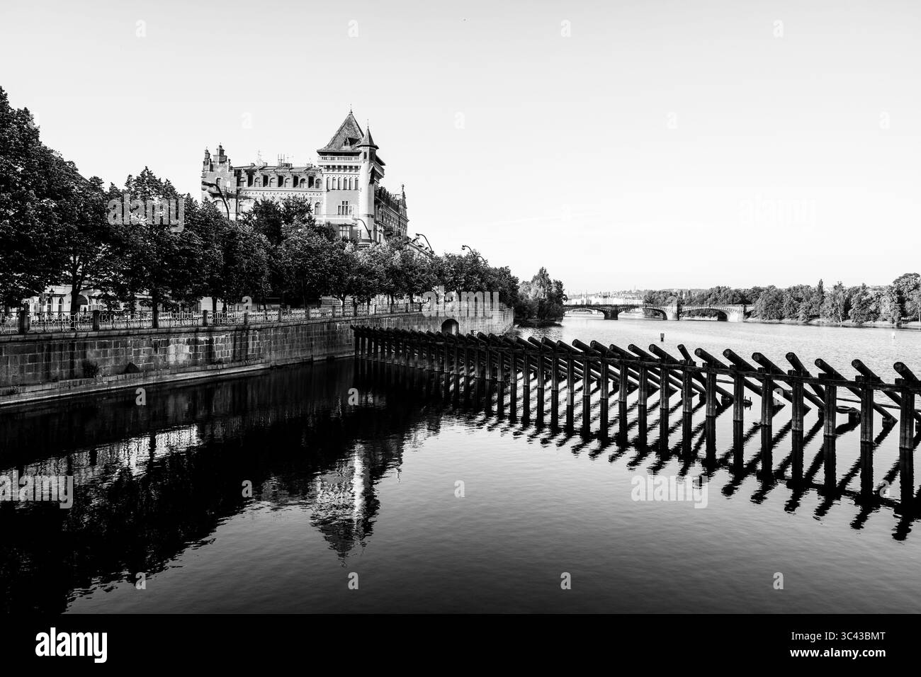 Les visiteurs se promènent le long du quai de Smetana à Prague, en admirant les eaux tranquilles de la rivière Vltava et l'architecture historique en arrière-plan par temps clair. Banque D'Images