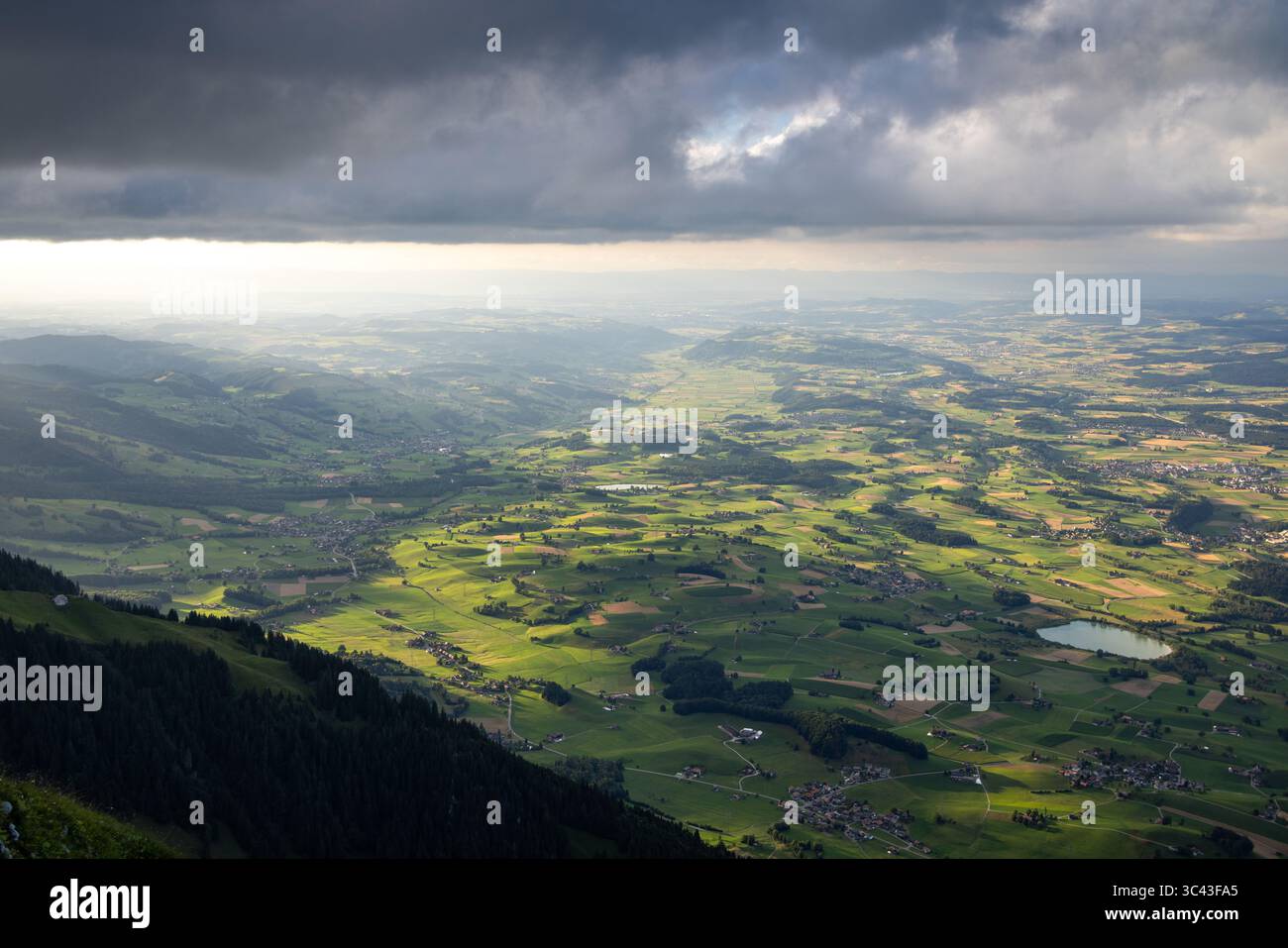 Une vue aérienne panoramique capture une vallée luxuriante et verdoyante creusée par le fleuve Aar en Suisse. Des nuages sombres et dramatiques se dessinent au-dessus de nous, partiellement illuminés Banque D'Images