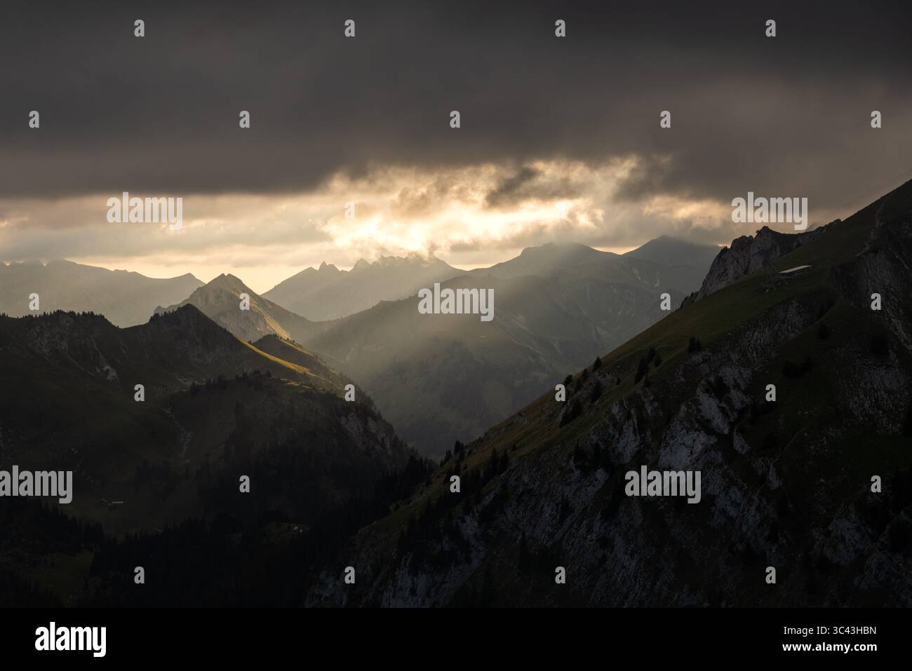 Une photographie de paysage spectaculaire capture la chaîne de montagnes Alpen à l'aube. La lumière dorée traverse les nuages, illuminant les sommets et les vallées. Banque D'Images