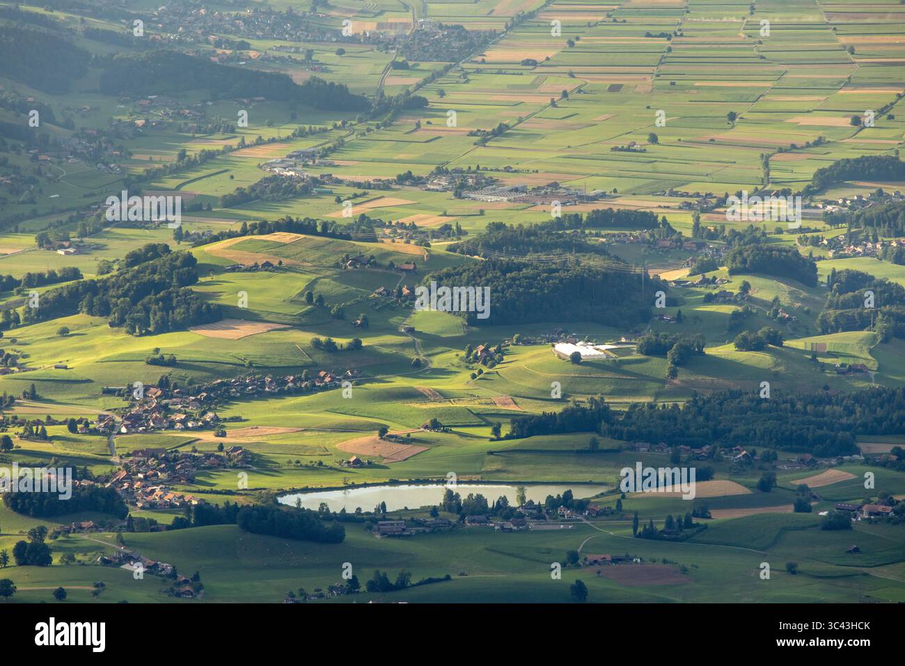 Une vue aérienne capture un paysage suisse tranquille caractérisé par de douces collines verdoyantes et un petit lac calme niché dans la vallée. Le s Banque D'Images